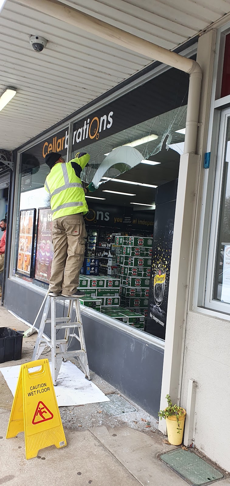 Smashed shopfront window with a glazier on a ladder removing the broken glass