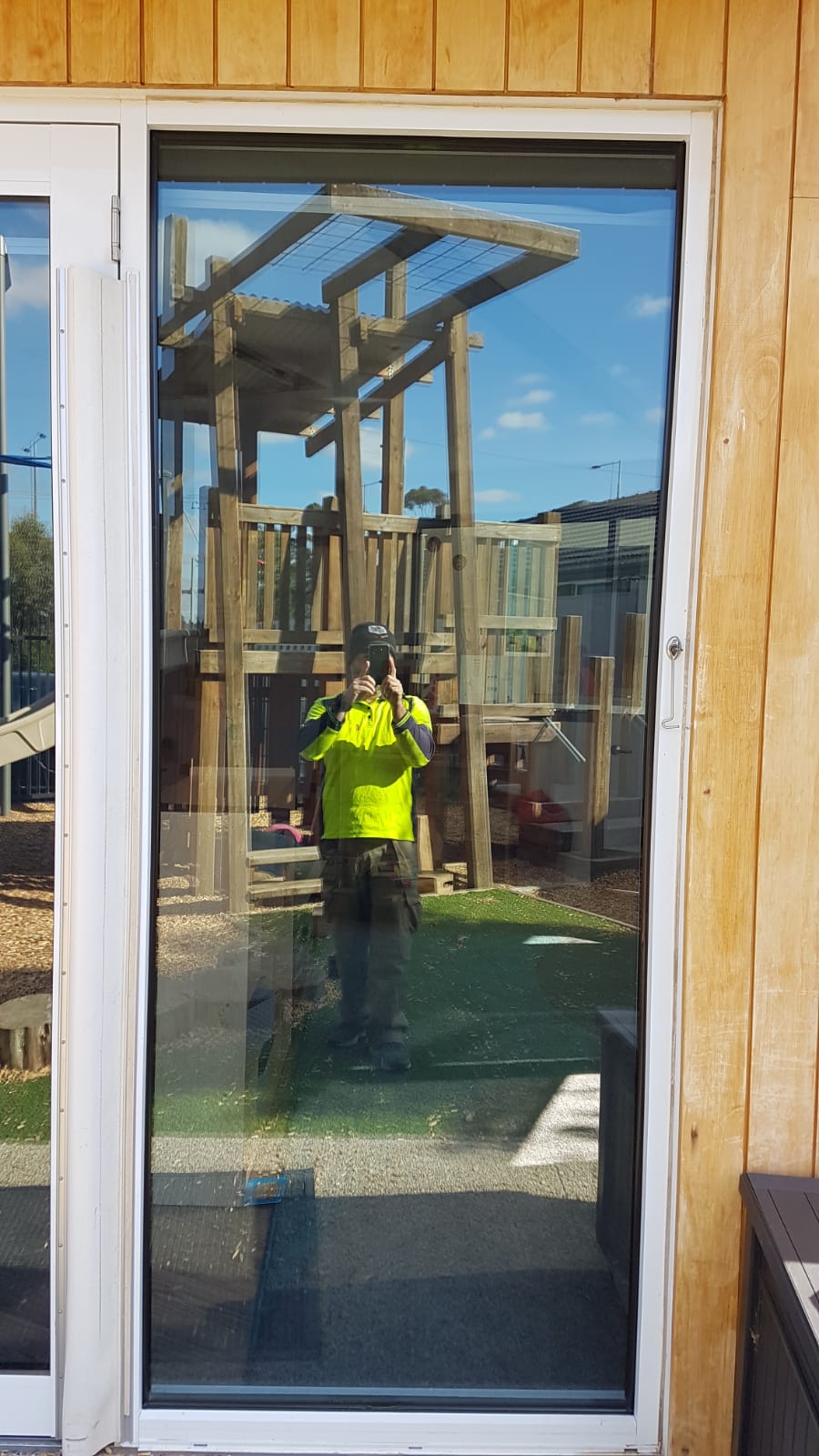 A new full-height glass pane fitted beside a timber wall, with a playground reflected outside