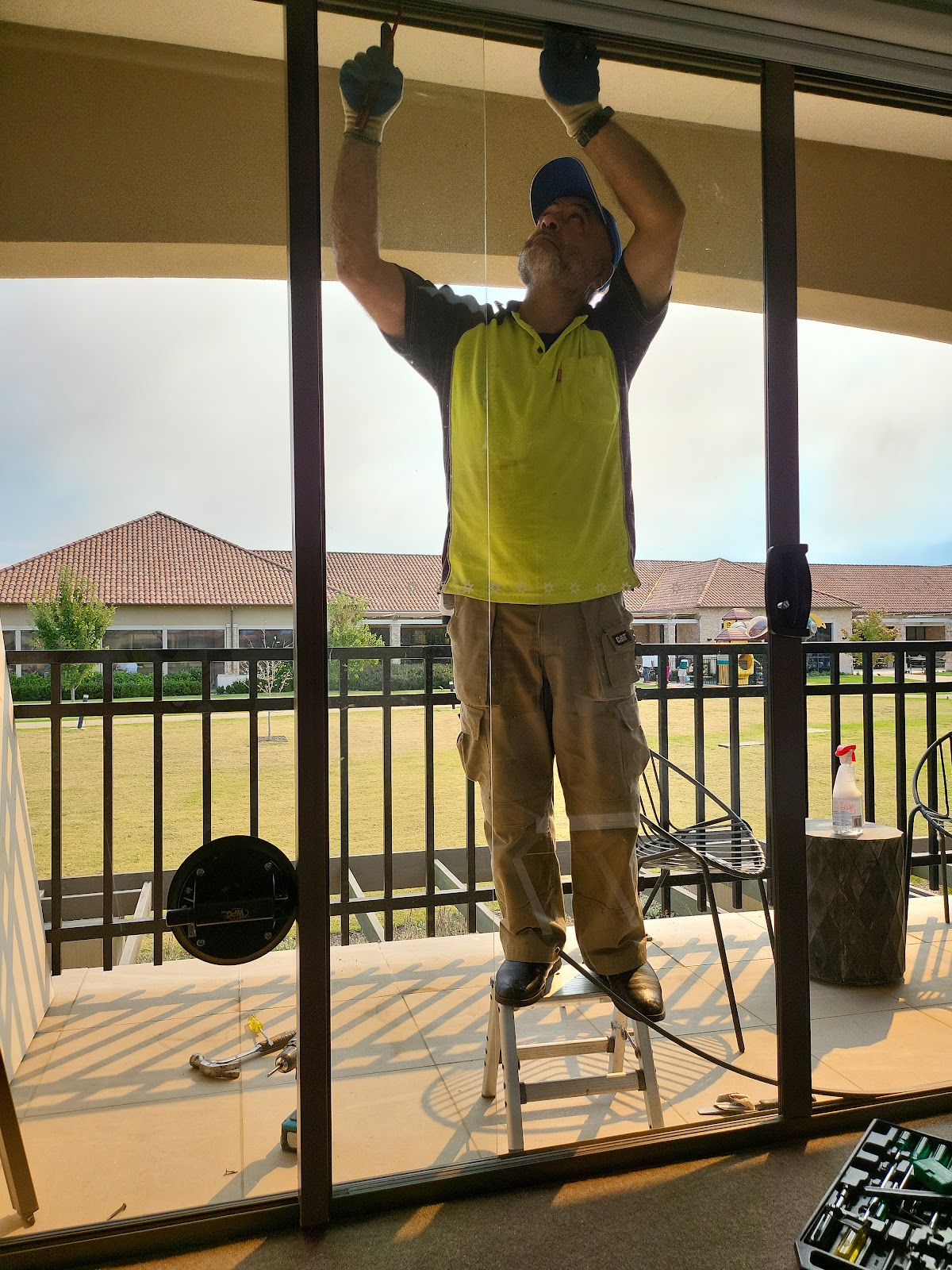 Mansour on a step ladder fitting glass into a sliding door on a balcony